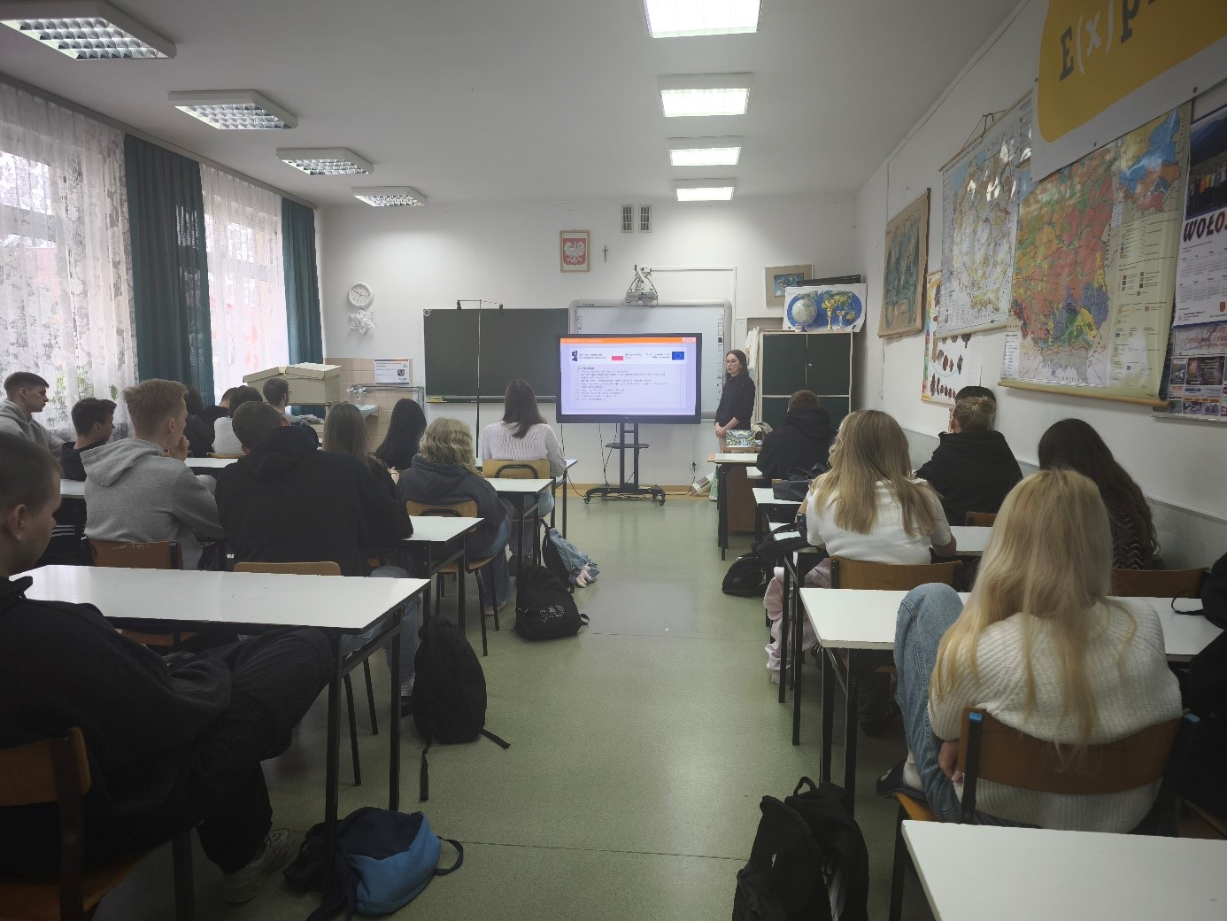 Na zdjęciu widoczna jest sala dydaktyczna. Uczniowie szkoły słuchają wykładu prowadzonego przez przedstawicielkę UJK. Widoczna jest także wyświetlona prezentacja multimedialna, którą oglądają uczestnicy spotkania.