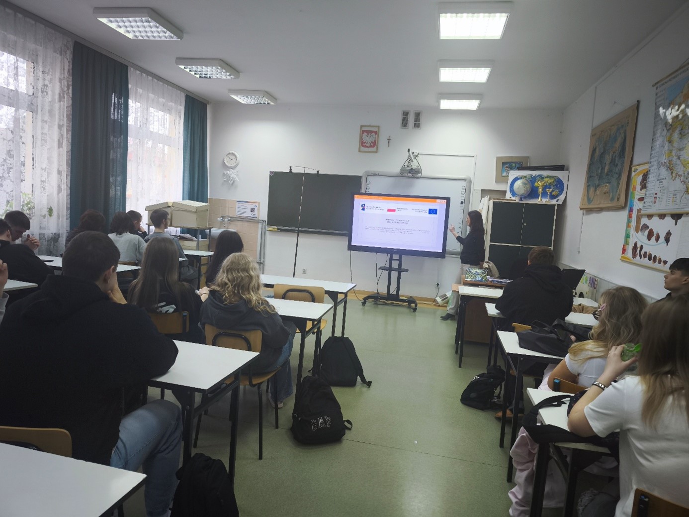 Na zdjęciu widoczna jest sala dydaktyczna. Uczniowie szkoły słuchają wykładu prowadzonego przez przedstawicielkę UJK. Widoczna jest także wyświetlona prezentacja multimedialna, którą oglądają uczestnicy spotkania.