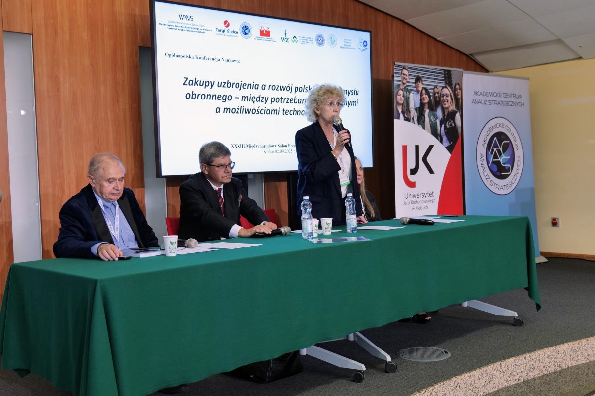 Spotkanie panelowe z trzema osobami przy stole. W tle ekran z prezentacją.