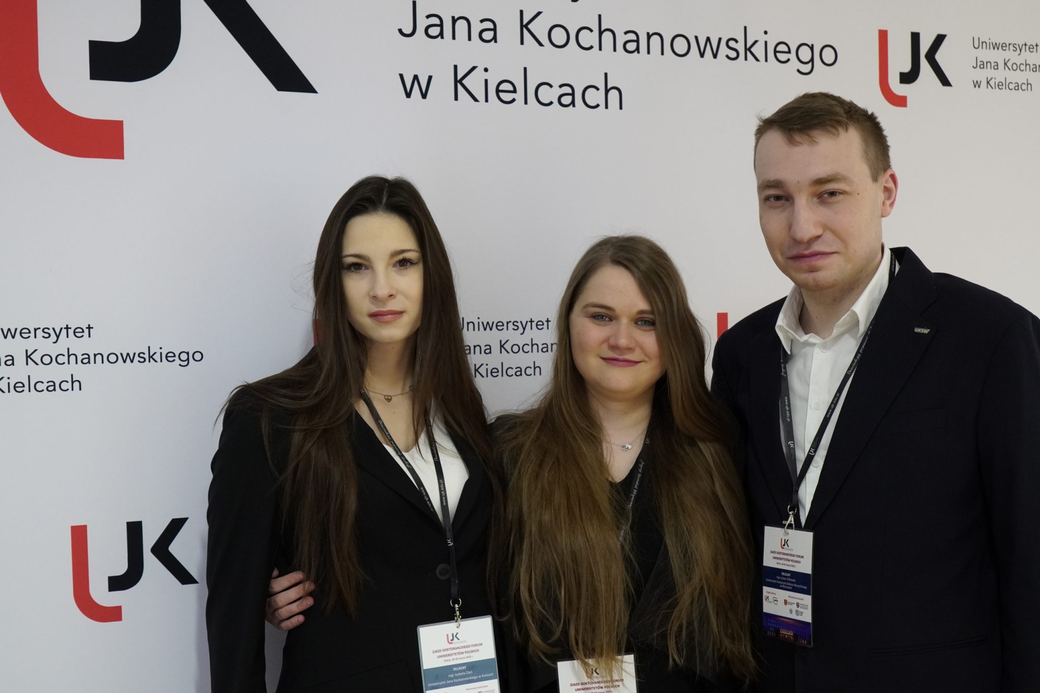 Uczestnicy spotkania na tle ścianki reklamowej UJK.