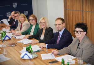 Grupa osób siedzących przy stole konferencyjnym, uśmiechniętych, z dokumentami podczas spotkania