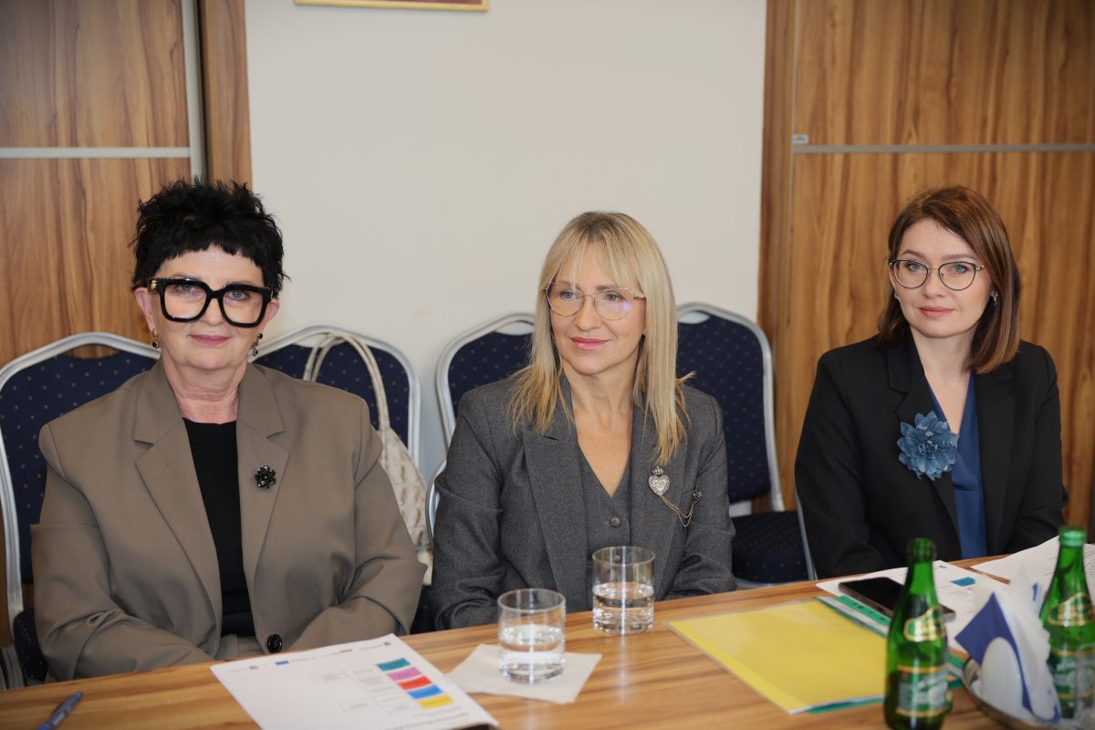 Trzy kobiety w eleganckich garniturach siedzą przy stole konferencyjnym z dokumentami