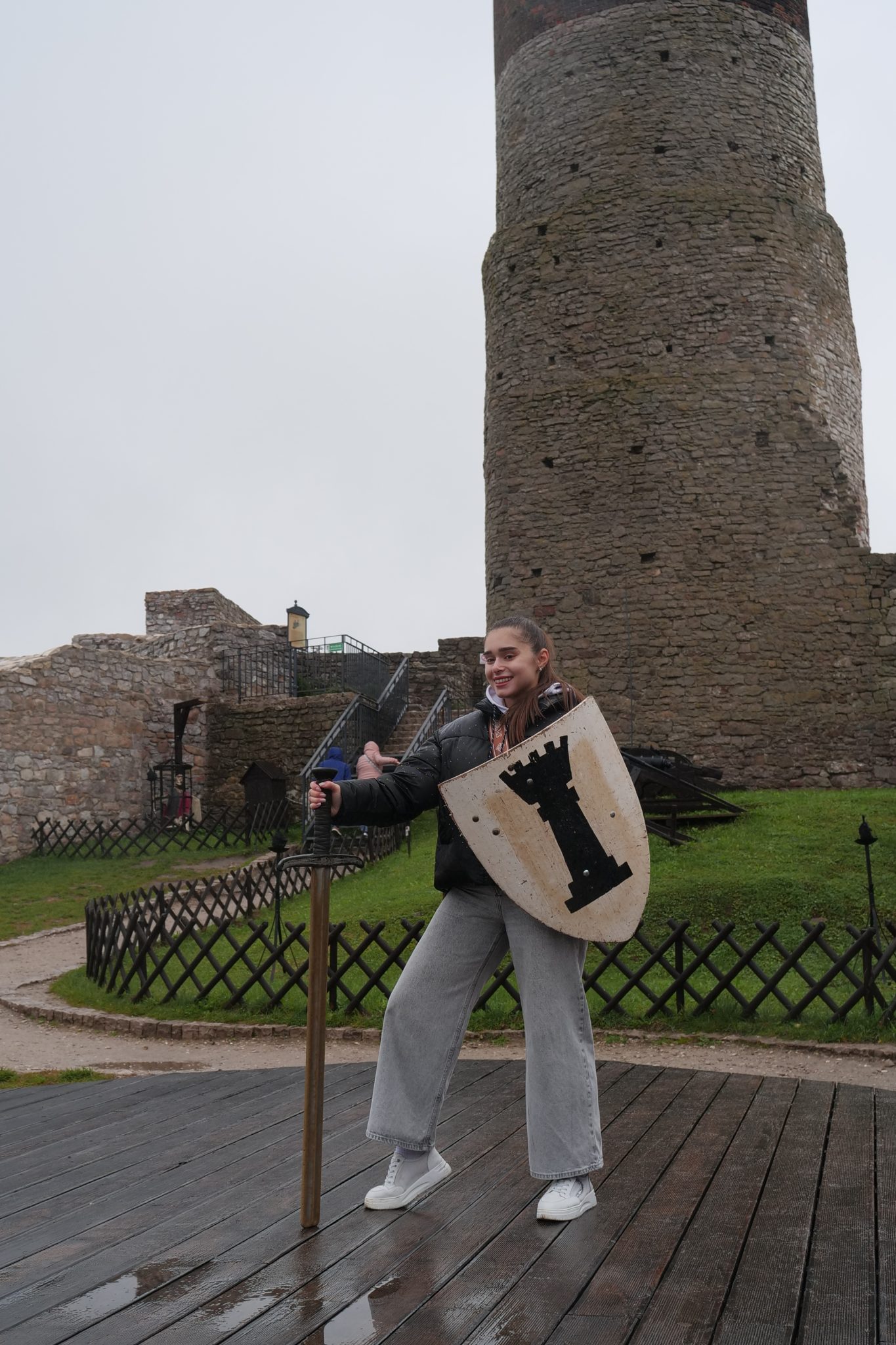 Studentka wymiany międzynarodowej z mieczem i tarczą na tle Zamku Królewskiego w Chęcinach.