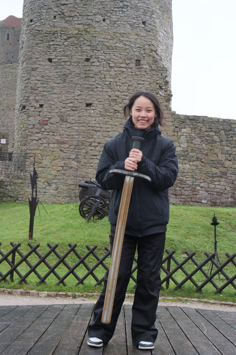 Studentka wymiany międzynarodowej z mieczem na tle Zamku Królewskiego w Chęcinach.