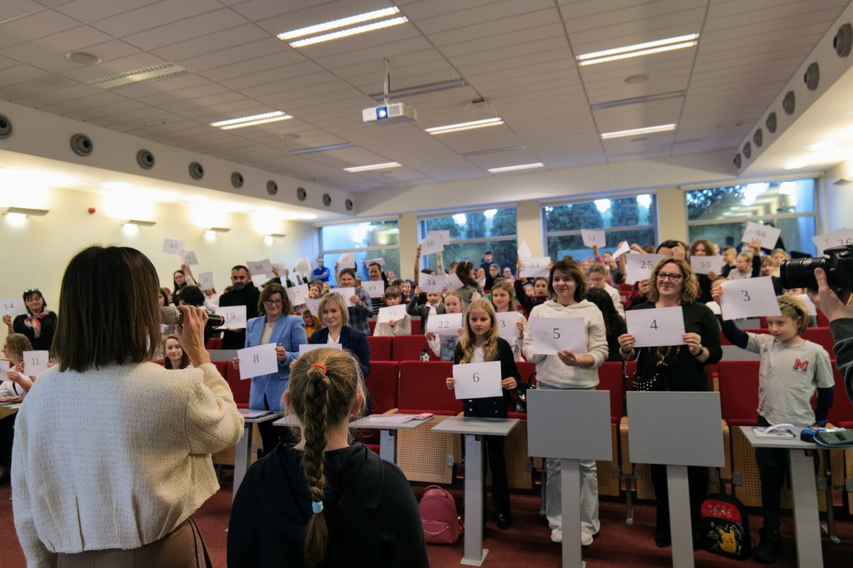 Prowadząca wykład, a uczestnicy spotkania z kartkami papieru.