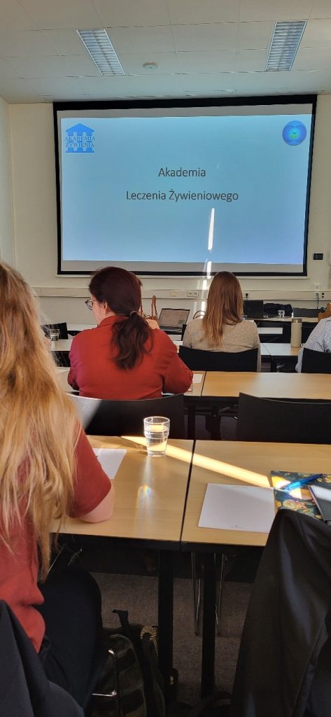 Na zdjęciu widać salę ćwiczeniową, Uczestnicy siedzą w ławkach tyłem do zdjęcia. Patrzą na wyświetlaną prezentację.