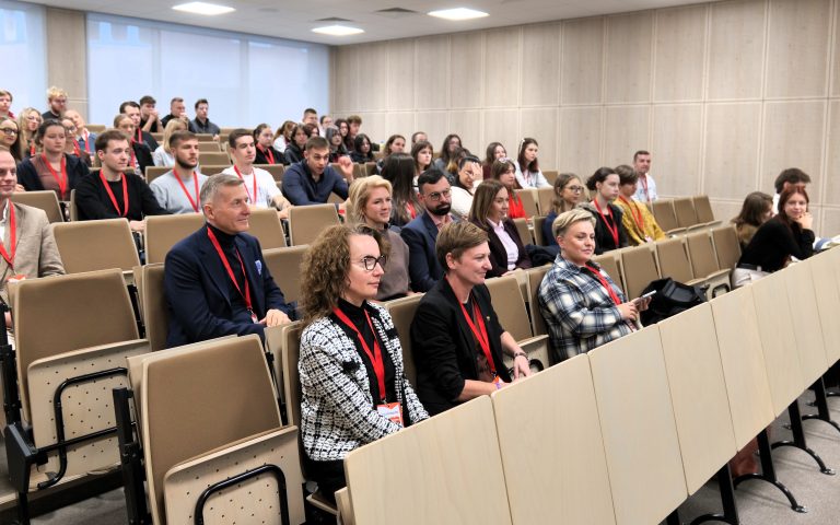 Wiele osób zajmujących miejsca na sali wykładowej