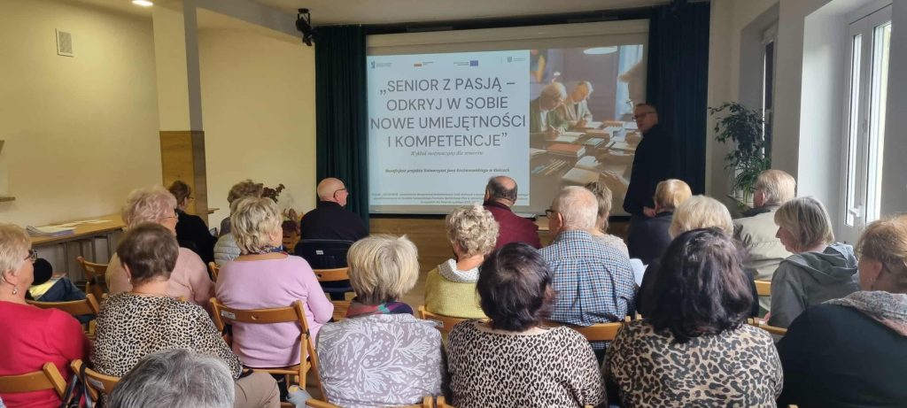 Prowadzący oraz uczestnicy wykładu widziani z końca sali. W tle ekran prezentacji.