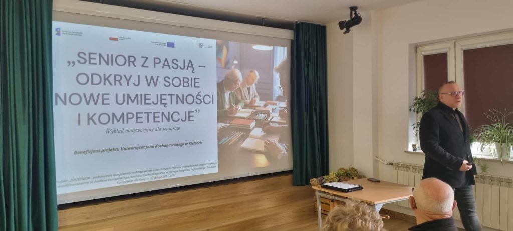 Prowadzący w trakcie wykładu. W tle plansza "senior z pasją - odkryj w sobie nowe umiejętności i kompetencje"