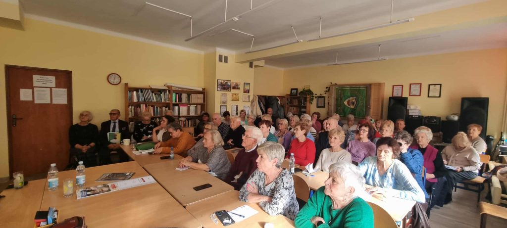 Sala wypełniona uczestnikami wykładu, siedzącymi w ławkach