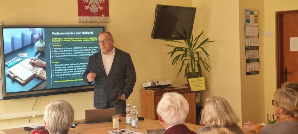 Prowadzący oraz uczestnicy wykładu w tle widać jeden ze slajdów prezentacji