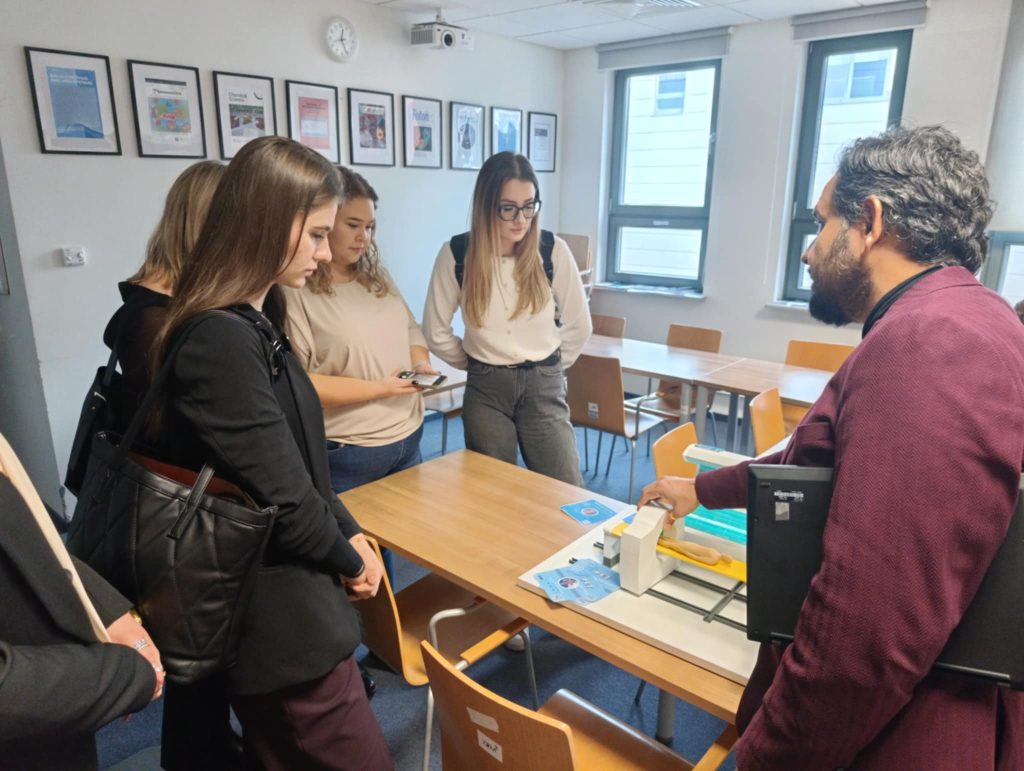 Na zdjęciu widać jak przedstawiciel instytucji przyjmującej prezentuje studentkom praktyczną stronę badań nad nowoczesnymi metodami obrazowania.