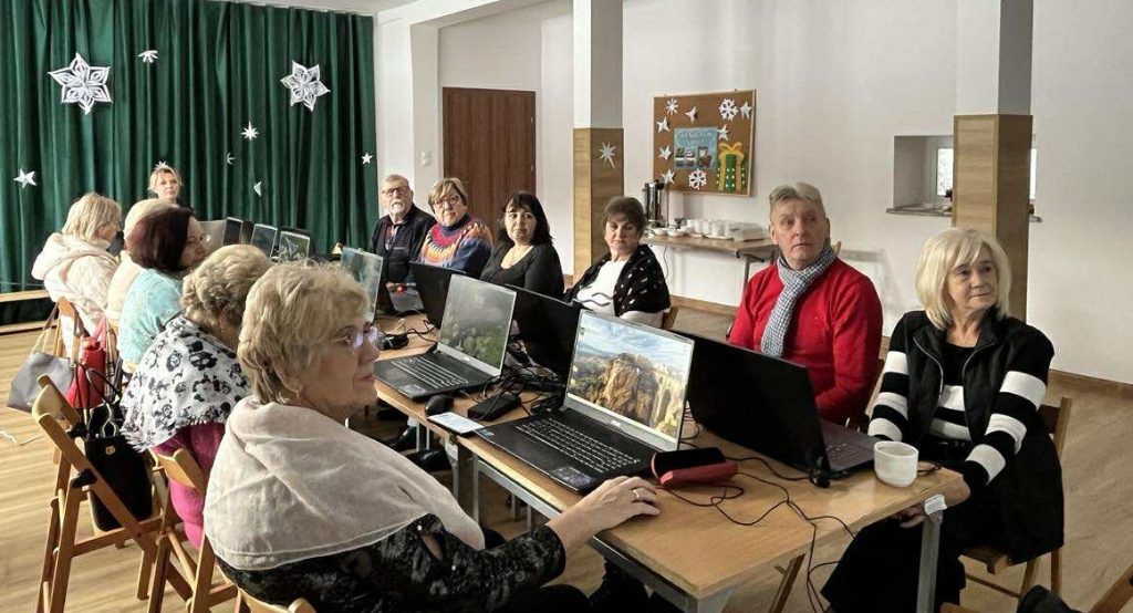 Uczestnicy (seniorzy) z gminy Masł&oacute;w podczas zajęć cyfrowych pracują przy laptopach pod nadzorem trenera UJK - 3