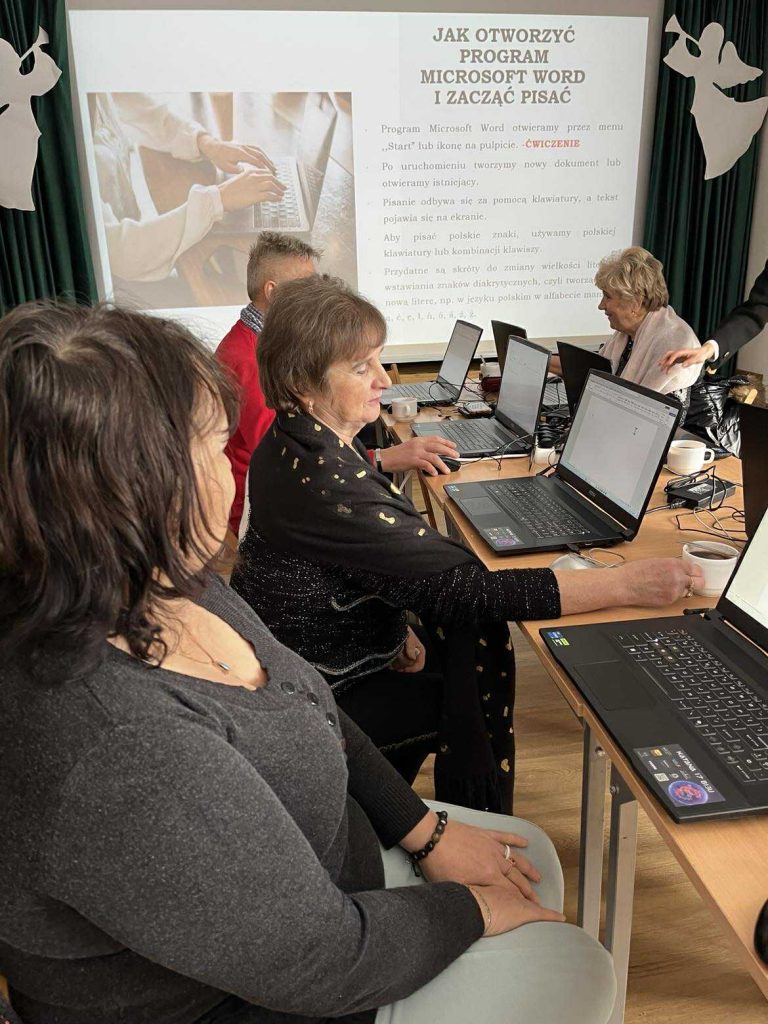 Uczestnicy (seniorzy) z gminy Masł&oacute;w podczas zajęć cyfrowych pracują przy laptopach pod nadzorem trenera UJK - 4