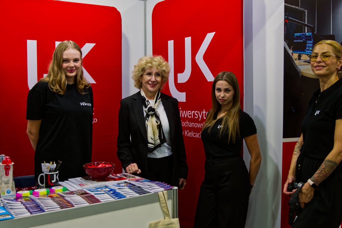 Zapytanie zostało przetworzone Treść wiadomości Gemini Stoisko promocyjne Uniwersytetu Jana Kochanowskiego w Kielcach. Cztery uśmiechnięte kobiety (jedna w białej apaszce, pozostałe w czarnych koszulkach z logo UJK) stoją przy stole z ulotkami i gadżetami. W tle duże czerwone panele z białym logo uczelni.