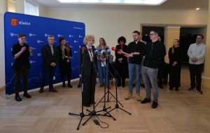 Uczestnicy spotkania na tle ścianki reklamowej. 