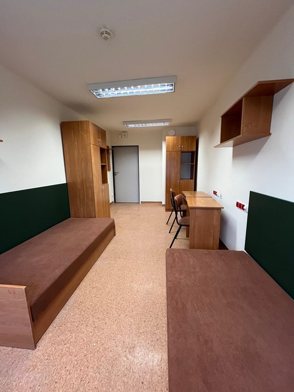 Pok&oacute;j dwuosobowy w domu studenta Fama. W pomieszczeniu znajdują się dwie brązowe szafy, p&oacute;łki ścienne oraz dwa ł&oacute;żka w ciemnobrązowym kolorze. Podłoga jest jasnobrązowa, a wnętrze przestronne i dobrze oświetlone.