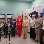 Uczestnicy konferencji prasowej w sali dydaktycznej z ekranami medycznymi. Dziewięć osób stoi w rzędzie przed mikrofonami. W tle ścianka z logo Urzędu Marszałkowskiego Województwa Świętokrzyskiego oraz banner Wydziału Lekarskiego UJK.