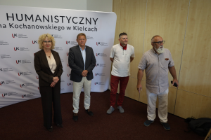 Czworo prelegentów stojących w rzędzie i pozujących do zdjęcia na tle ścianki Wydziału Humanistycznego Uniwersytetu Jana Kochanowskiego w Kielcach.