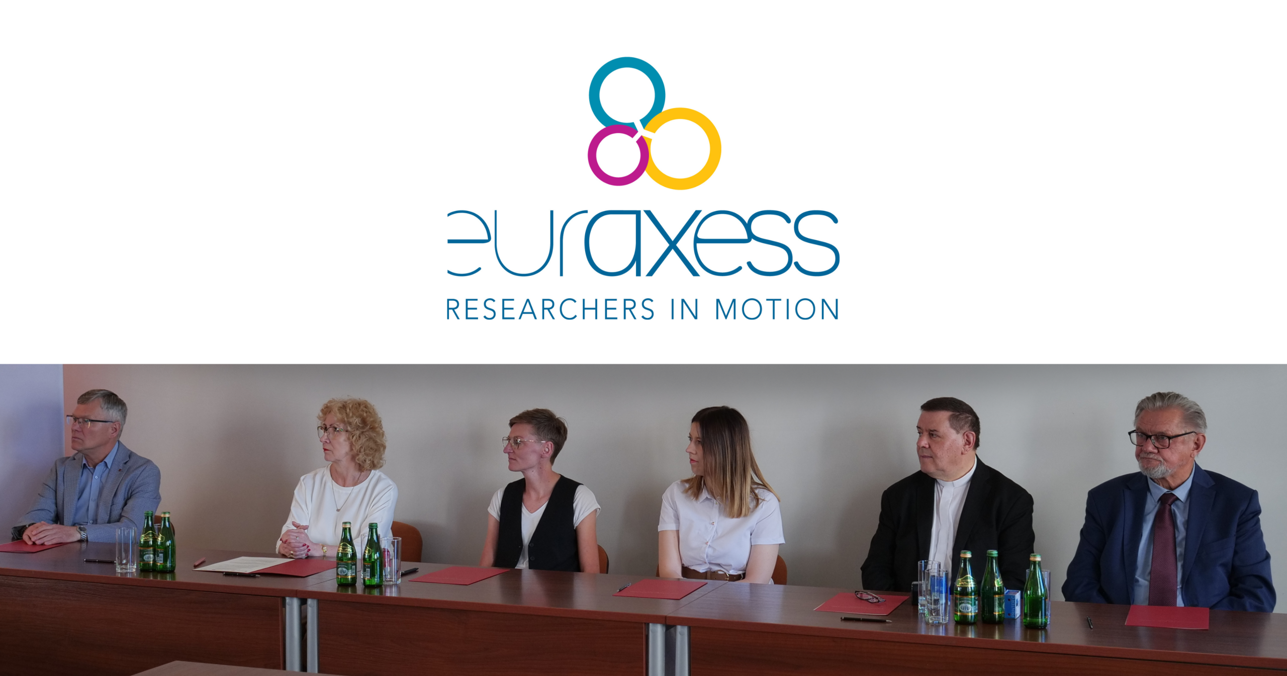 Uczestnicy spotkania siedzą przy stole konferencyjnym pod logo EURAXESS &bdquo;Researchers in Motion&rdquo;.