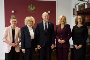 Pamiątkowe zdjęcie ambasadora w towarzystwie trzech kobiet na tle godła Polski.