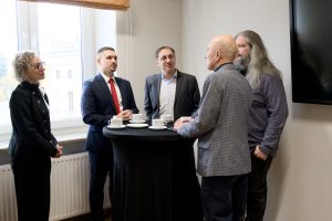 Pięcioosobowa grupa rozmawiająca przy kawie i wysokim stoliku.