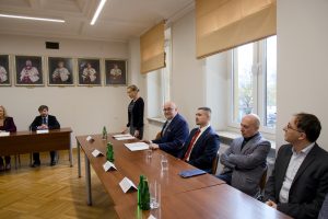 Kobieta stojąca przy stole prezydialnym oraz grupa mężczyzn przysłuchujących się jej przy bocznym stole konferencyjnym. JPG