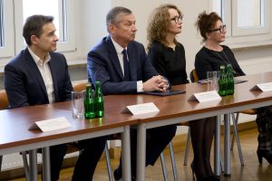 Czworo uczestników z uwagą przysłuchujących się obradom, siedzących przy długim stole z wodą i wizytówkami.