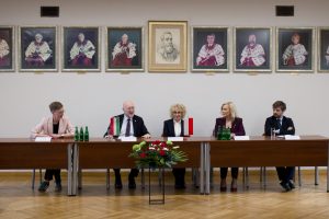 Ambasador i czworo ludzi siedzący razem przy głównym stole na tle ściany z portretami.