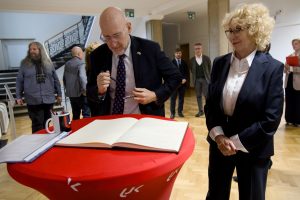 Ambasador z długopisem w dłoni, przygotowujący się do złożenia podpisu w księdze pamiątkowej leżącej na okrągłym stoliku.